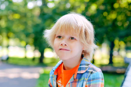 Cute blonde caucasian kid sitting on the bench at the park. Summer vacation happy childhood conceptの写真素材