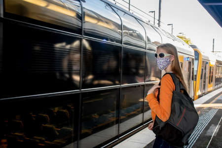 Teenage student girl wearing face mask waiting for the train on the station platform. Sydney trains transport NSW during Covid-19 pandemic. Mandatory face masks in public transportの写真素材