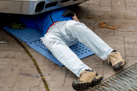 Garage mechanic. Man male wearing jeans underneath a car working on repairs. DIY car vehicle repair maintenanceの写真素材