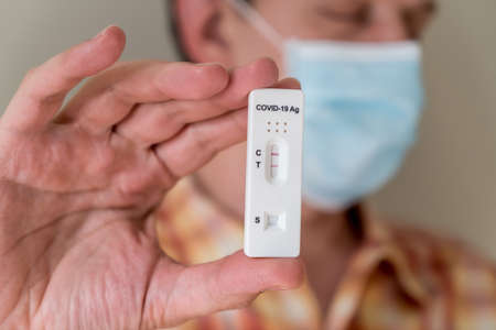 Man wearing face mask holding Covid-19 rapid antigen test cassette with negative result of rapid diagnostic test. Self-testing kit at homeの写真素材