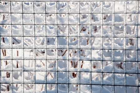 Winter background. Grid mesh fence covered with snow and ice after the snowfall in the countryside. Beautiful winter timeの写真素材