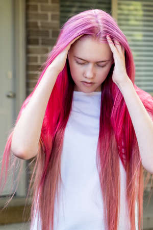 Unhappy stressed sad teenage girl with bright raspberry pink ombre long colored hair. Generation Z,...