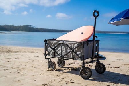 Outdoor beach cart wagon and beach umbrella on a sandy beach near the ocean. Family vacation holidays conceptの写真素材