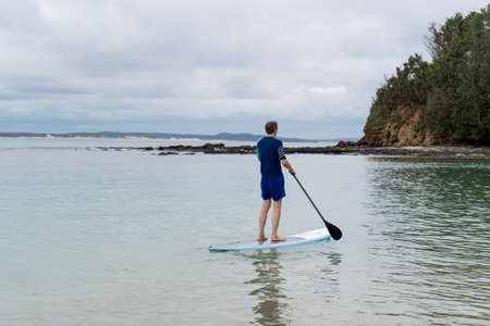Man wearing rash guard on a stand-up paddle board at the ocean bay in Australia. SUP water sport activity SUP water sport summer activityの写真素材