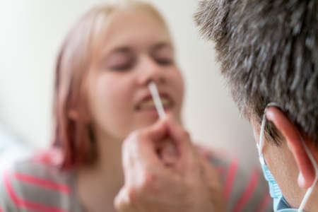 Selective focus bokeh shot of man wearing face mask and teenage girl while doing rapid antigen test...
