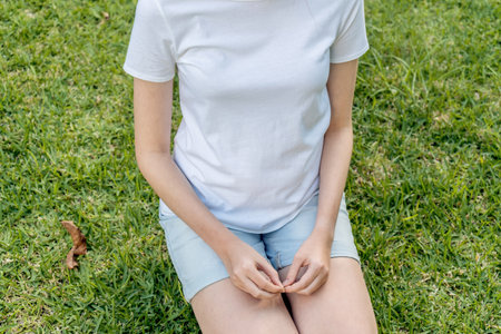 Girl wearing mockup white t-shirt and blue denim shorts sitting on a green grass. Template fashion copy spaceの写真素材