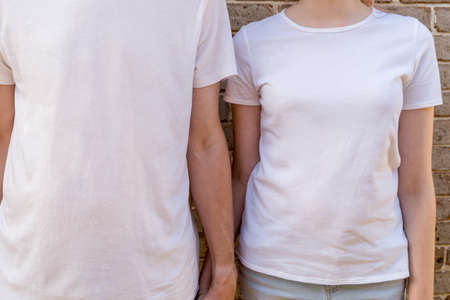 Couple wearing mockup white t-shirts on brick wall background holding hands. Template copy space fashionの写真素材