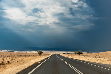 Straight open empty road surrounded by farms and fields just before the storm in Australia. Road trip travel conceptの写真素材