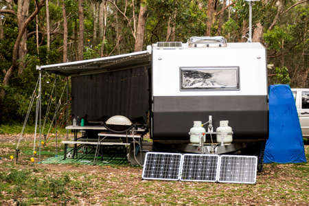 RV caravan camper on a campsite in the bush forest nature. Awning, portable toilet, solar panels, bbq, table. Family camping set upの写真素材