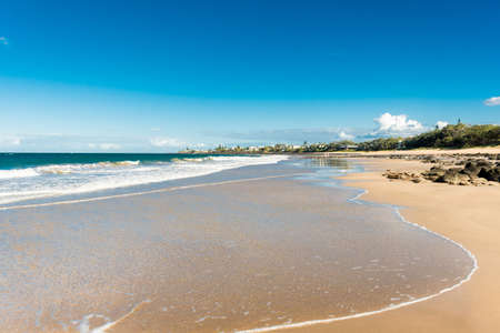 Beautiful ocean sandy beach nature background with town on the horizon. Ocean tide. Kellys Beach, Queensland, Australiaの写真素材