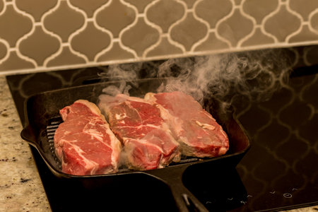 Grilling cooking new york beef strip sirloin steaks on cast iron grill pan skillet on a electric ceramic stove counter top at homeの写真素材