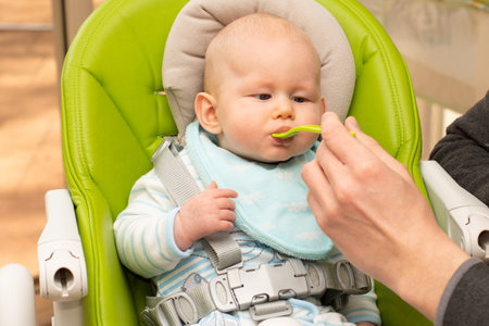 Feeding little baby with spoon full of baby apple puree porridge. Baby first solids. Weaning.