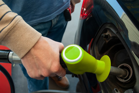 A man hand holding pump filling gasoline. Pumping petrol into the tank. A red car refuel on gas petrol stationの写真素材