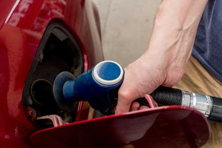 A man hand holding pump filling gasoline. Pumping petrol into the tank. A red car refuel on gas petrol stationの写真素材