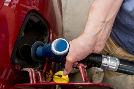 A man hand holding pump filling gasoline. Pumping petrol into the tank. A red car refuel on gas petrol stationの写真素材
