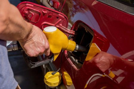 A man hand holding pump filling gasoline. Pumping petrol into the tank. A red car refuel on gas petrol stationの写真素材