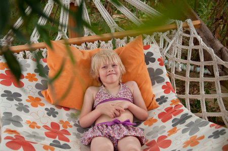 Summer beach tropical vacation with kids. Cute happy little caucausian girl rest laying in a hammockの写真素材