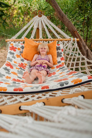 Summer beach tropical vacation with kids. Cute happy little caucausian girl rest laying in a hammockの写真素材