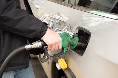 A man hand holding pump filling gasoline. Pumping petrol into the tank. A red car refuel on gas stationの写真素材