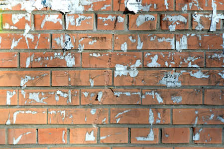 Old orange brick wall. Painted distressed wall surface. Vintage red brick wall with signs of old ads on it. Urban photo background for design. Building Facade With Damaged Plaster.の写真素材