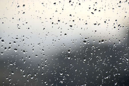 Abstract photo background. Rain drops on window. Selective focus, rainy city background. Water drops on glass. Rainy weather, blur wallpaper.の写真素材