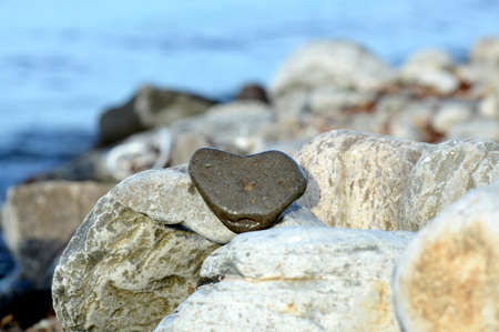 Heart shape stone against background of beach. Summer sunny day. Love, wedding and Valentine day concept. Finding beautiful and interesting stones. Beach vacation.の写真素材