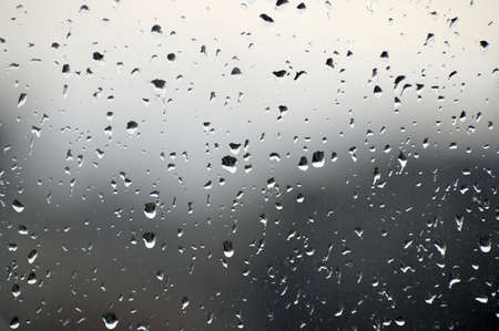 Abstract photo background. Rain drops on window. Selective focus, rainy city background. Water drops on glass. Rainy weather, blur wallpaper.の写真素材