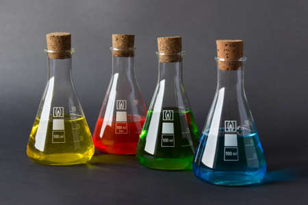 Four laboratory flasks with cork plugs and colorful liquids isolated on dark background.の写真素材