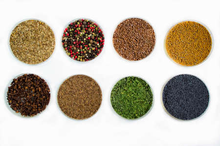 Herbs and seasonings - dried coriander, peppercorn, flax seeds, mustard, clove, cumin, parsley and poppy seeds in a transparent dish isolated on white background.の写真素材