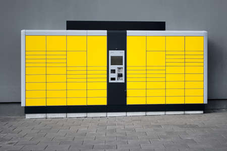 Yellow self-service parcel terminal on the background of gray wall and pavement.の写真素材
