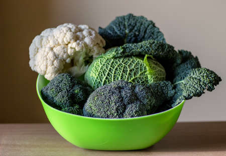 Organic vegetables - savoy cabbage, broccoli, white cabbage in a green bowl on the wooden table on white background. Set of various types of cabbages.の写真素材