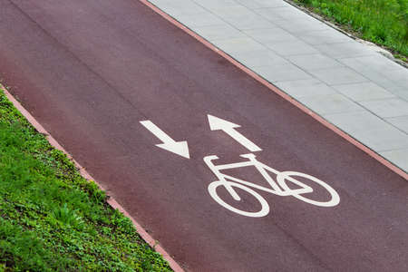 Bicycle lane signs with arrows on the red city bike pathway.の写真素材