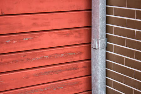 Materials of building exterior. Texture of wooden red wall planks with brown bricks and metal water pipe.の写真素材