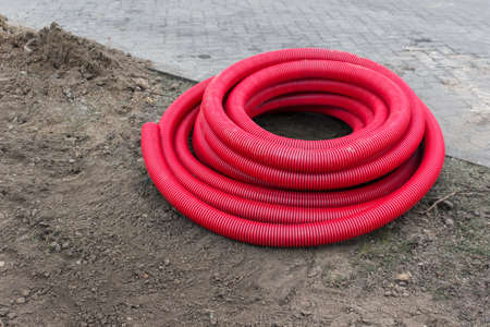 Red plastic pipes for underground electrical wires lying on the ground ready to be installed.