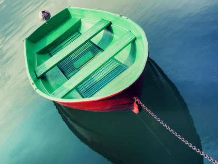 Single fishing boat painted in green color floating on water and tied with metallic chain.の写真素材