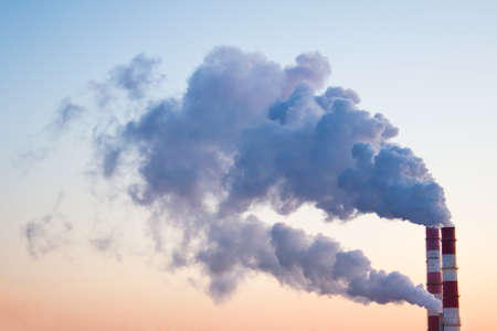 Smoke, fumes coming out of pipes of factory producing heat for central heating in winter on the background of skies.の写真素材