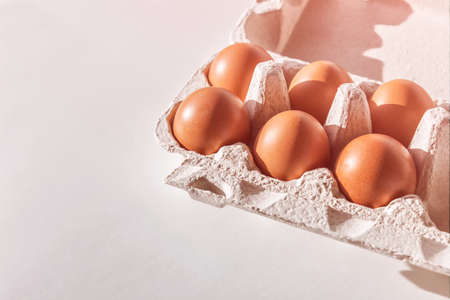 Six brown eggs in carton box on white background. Sunny photo for easter theme.の写真素材
