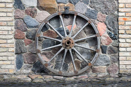 Large ancient wooden cart wheel attached to the wall made of stones.の写真素材
