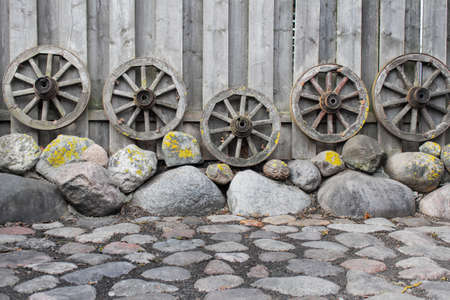 Backyard decoration with stones and ancient wooden cart wheels standing next to the fence.の写真素材