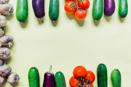 Background with various vegetables and copy blank space in the center of image. Flat lay with aubergine, zucchini, tomatoes and garlic on the light yellow background.の写真素材