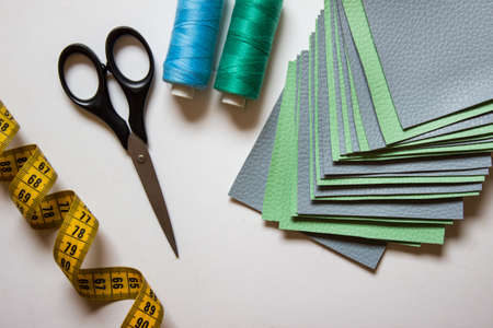 Green and blue colored sewing fabric samples with measuring tape, scissors and threads on white...