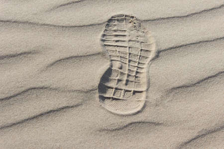 Single shoe footprint on wavy sand of the beach.