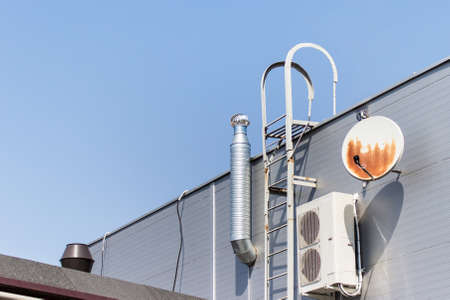 Building rooftop with metallic stairs, old weathered rusted satellite antennas and office ventilation air condition system.の写真素材