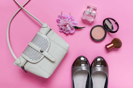 Composition with fashion accessories -  female summer small tote bag, shoes with golden decoration, one peony flower, perfume bottle, bronzer and facial brush arranged on pink background.の写真素材