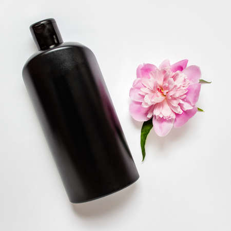 Black shapoo bottle with pink peony flower on white background.の写真素材