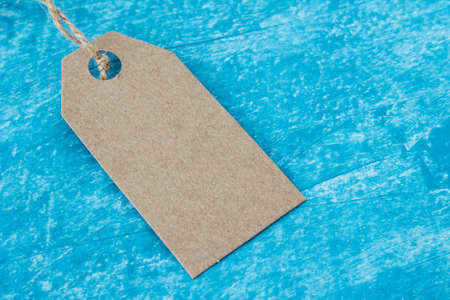 Mock up of craft paper tag label on creative textured blue acrylic paint backgound. Close up photo...