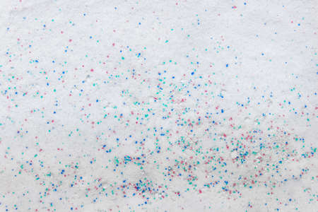 Top view of clothes white washing powder detergent with small blue red granules.