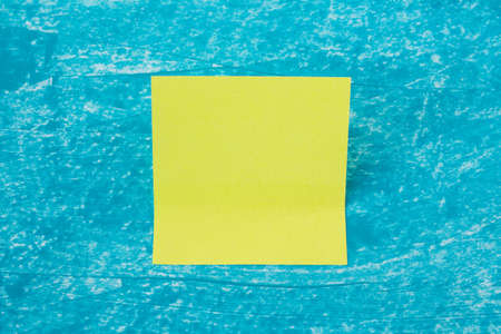 Single memo neon green stick note leaf on creative textured blue acrylic paint backgound. Close up...