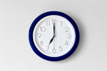 Large single round office clock showing seven o clock isolated on white background with blue detail...
