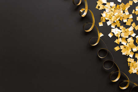 Decorative golden glitter confetti and spiral golden ribbon on black background.の写真素材